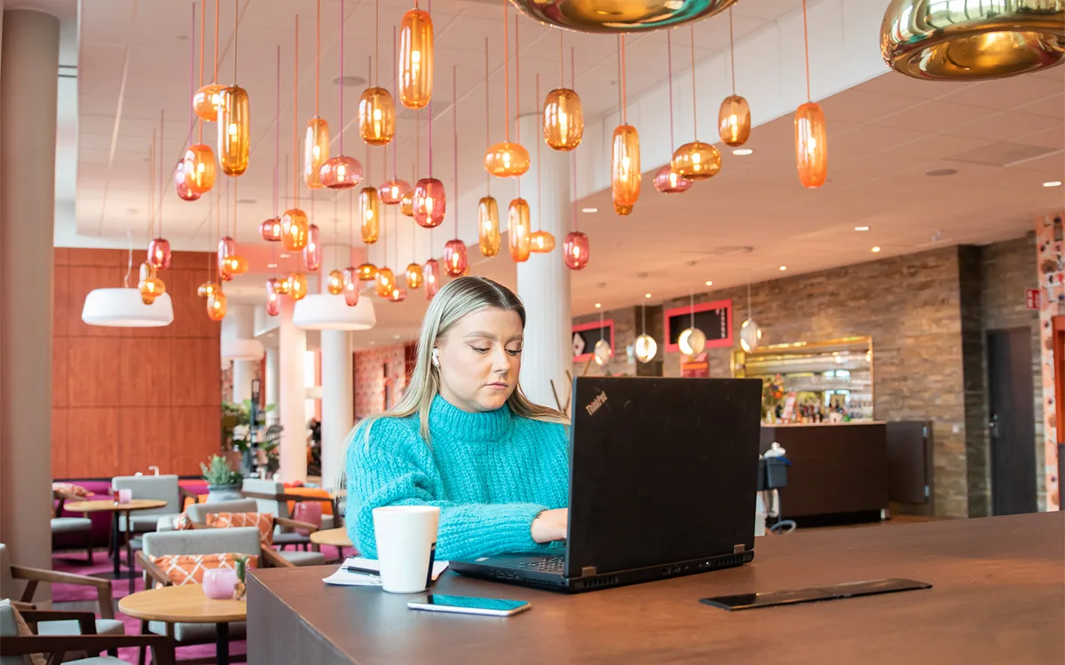 Woman working on laptop in hotel lobby with colorful lights on ceiling