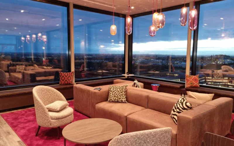 Hotellounge med soffa, bord och panoramafönster med utsikt i kvällsljus