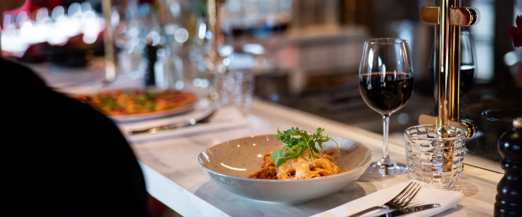 Pasta serverad i djup tallrik med glas rödvin på bardisk i restaurangmiljö