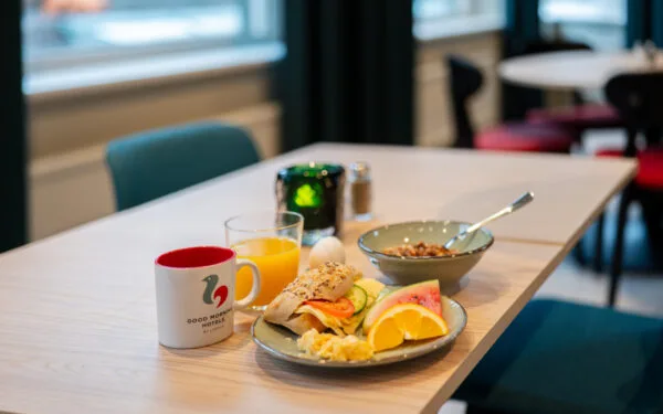 Frukosttallrik med fralla, frukt, crossiant. Skål med musli och yogurt, samt kaffe och juice.