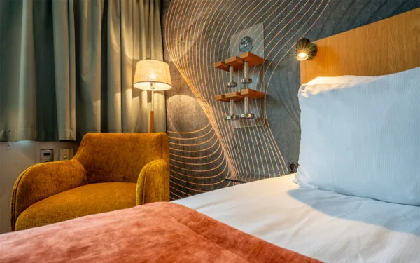 Närbild på säng och fåtölj i modernt hotellrum.