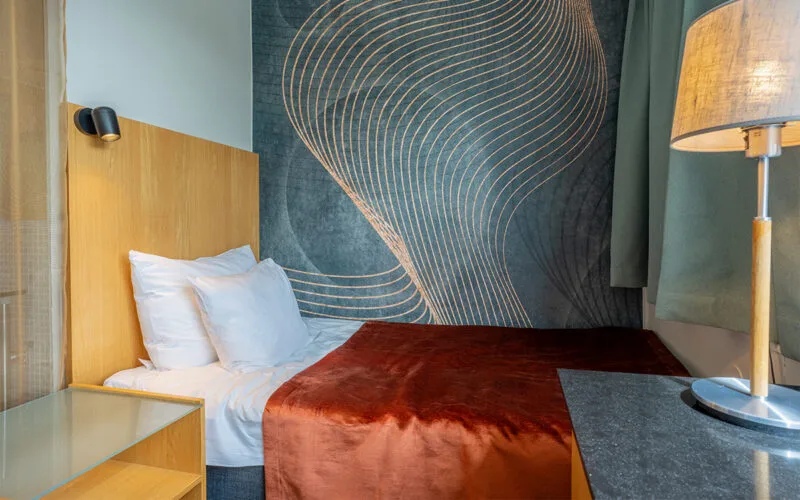 Hotellrum med dubbelsäng, trädetaljer och modern blå fondvägg.
