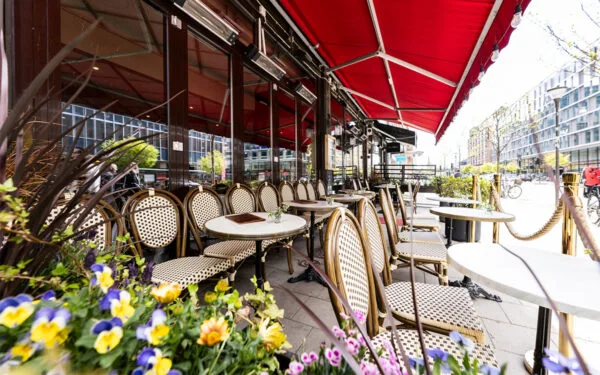 Uteservering med rottingstolar och röda markiser.