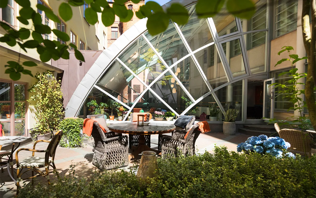Solbeskinnet gårdhave med havemøbler, grønne planter og glasfacade i baggrunden.