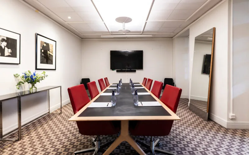 Mötesrum med långbord, röda stolar, block och pennor, samt stor skärm på väggen