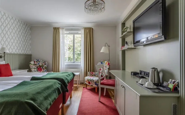 Hotellrum med säng, skrivbord och fåtölj vid fönster.