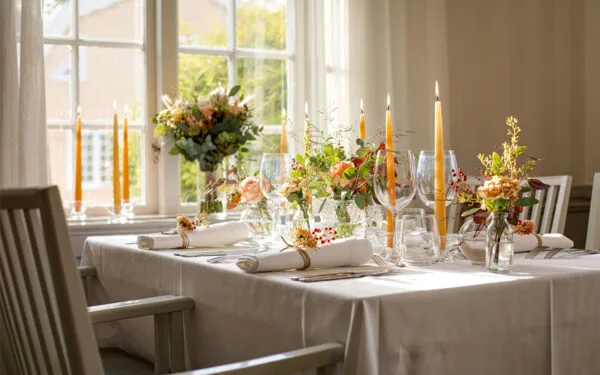 Dukat bord med blommor och tända ljus vid fönster.