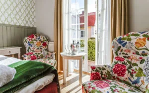 Hotellrum med blommiga fåtöljer, franska dörrar och utsikt mot innergård