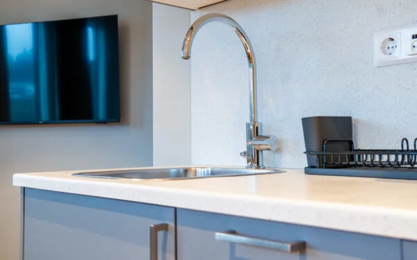 Kök i hotellrum med gråa detaljer och vit bänkskiva.