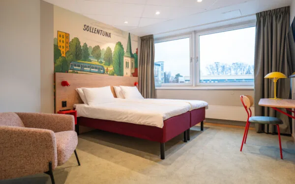 Hotellrum med säng, fotölj, heltäckningsmatta, mönstrad tapet på väggen