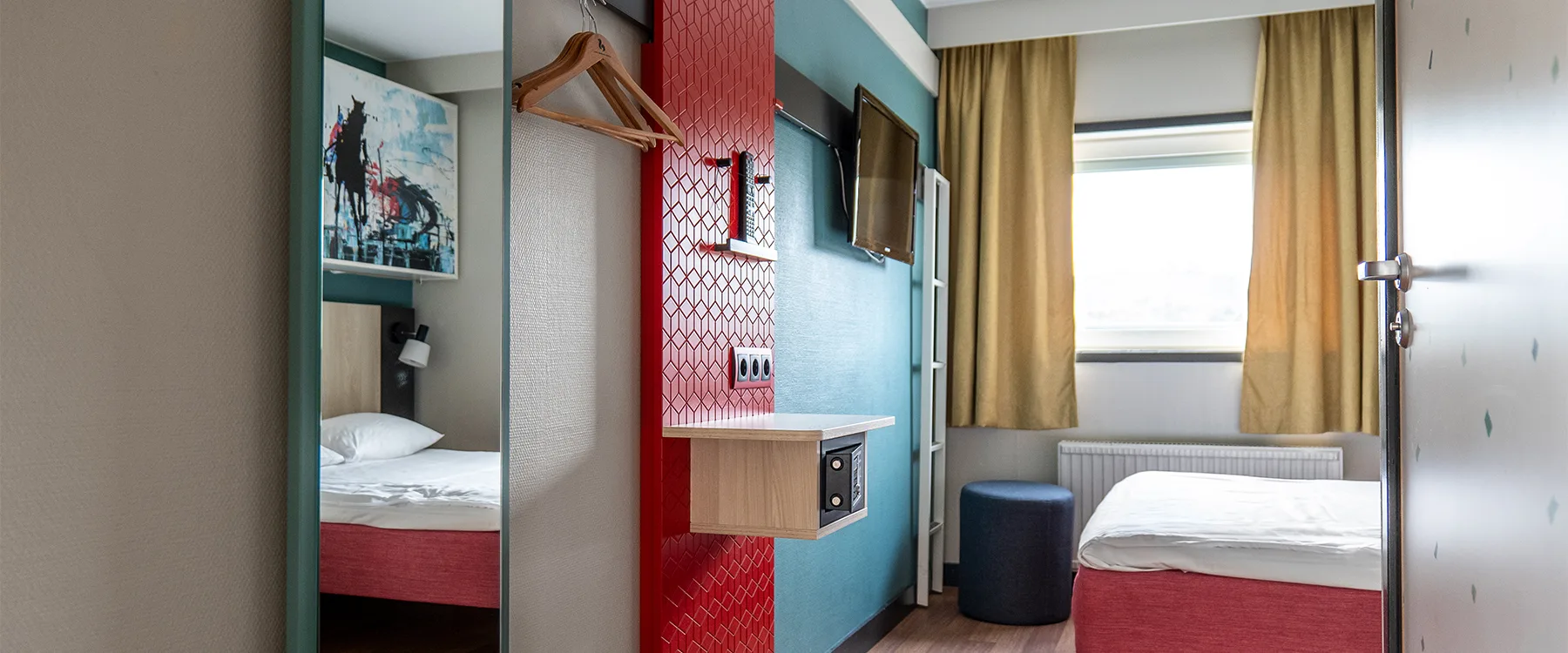 Hotellrum med färgglad inredning, vägg i rött och blått, tv och skrivbord.