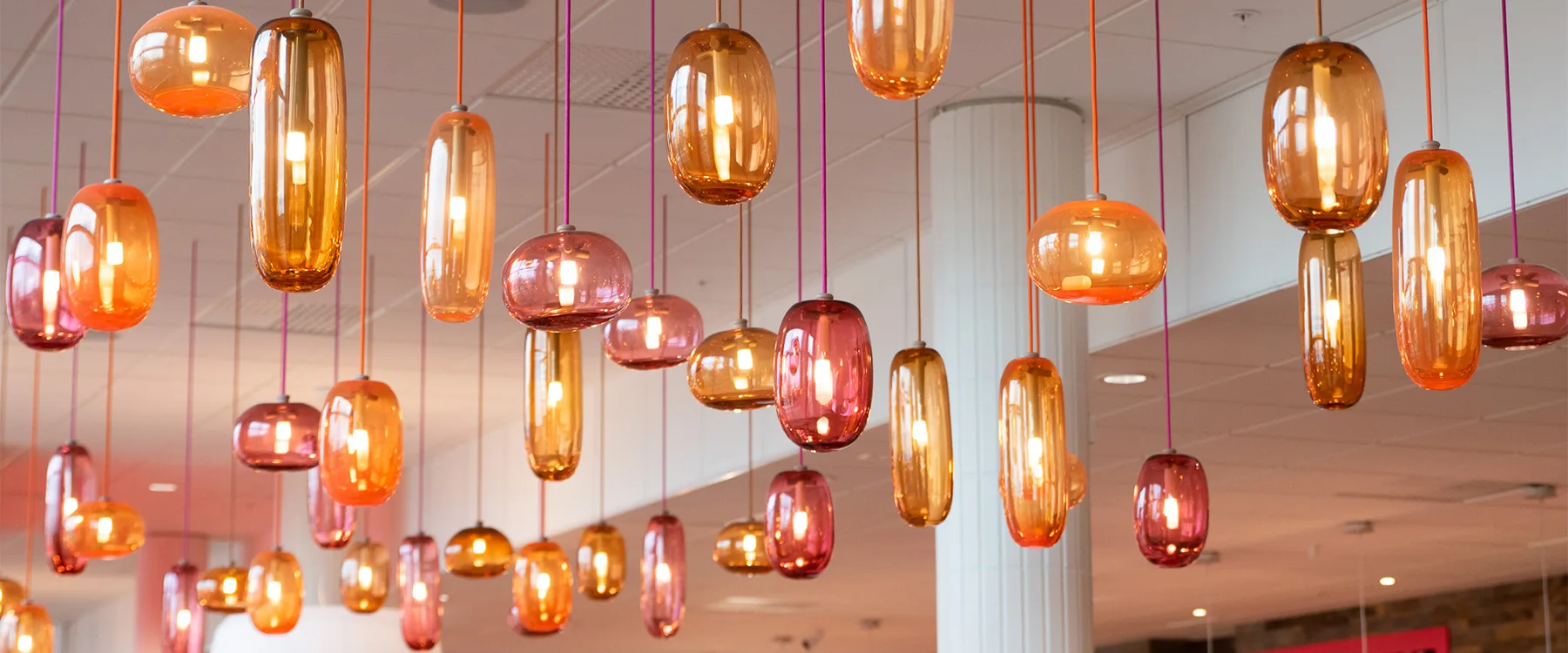 Flera hängande lampor i glas i varma färger.