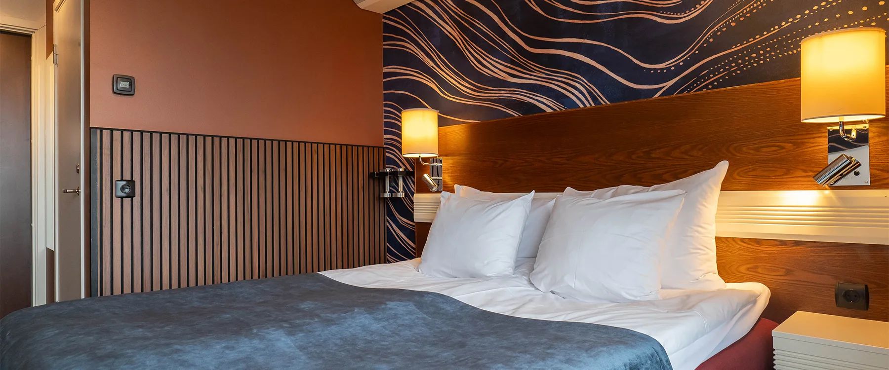 Hotellrum med bäddad säng, vita kuddar och dekorativ fondvägg.