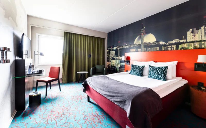 Hotellrum med dubbelsäng, skrivbord och gardiner