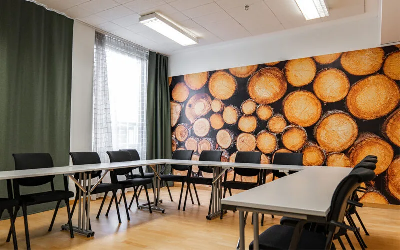 Konferensrum med U-formad möblering, svarta stolar och dekorativ vägg med trästammar