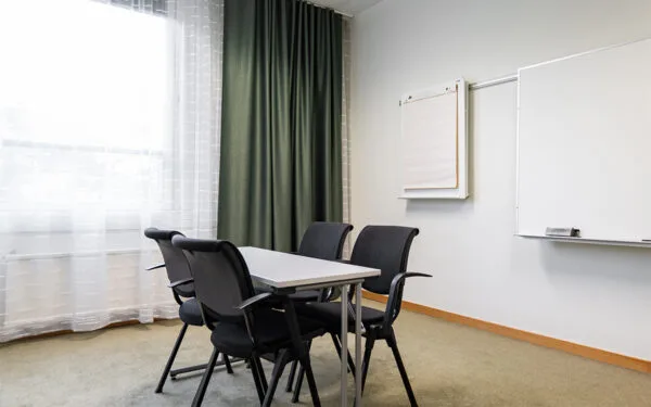 Mötesrum med litet bord, svarta stolar, whiteboard och blädderblock vid väggen.