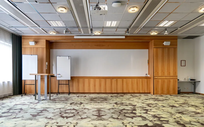 Konferensrum med scenyta, whiteboards, projektor i taket och träpanel vid väggen.