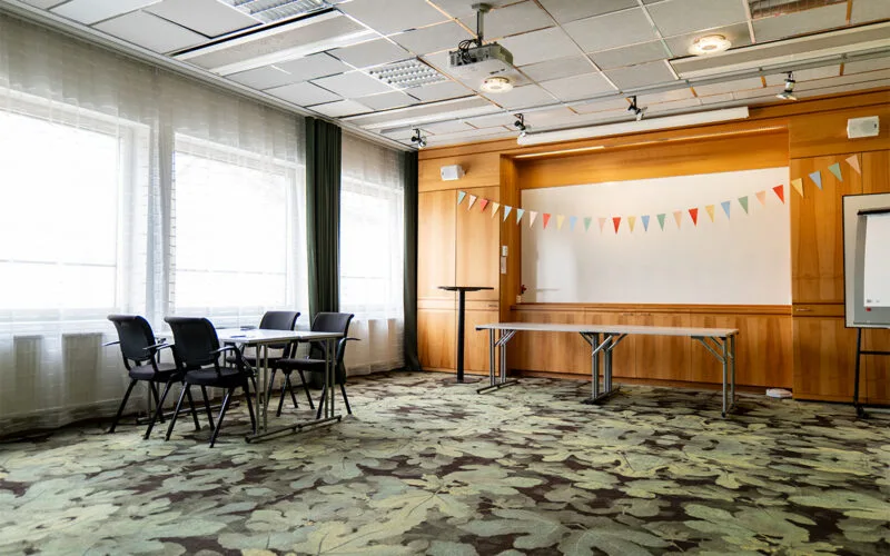 Konferensrum med scenyta, whiteboard, stolar och färgglada vimplar som dekoration.