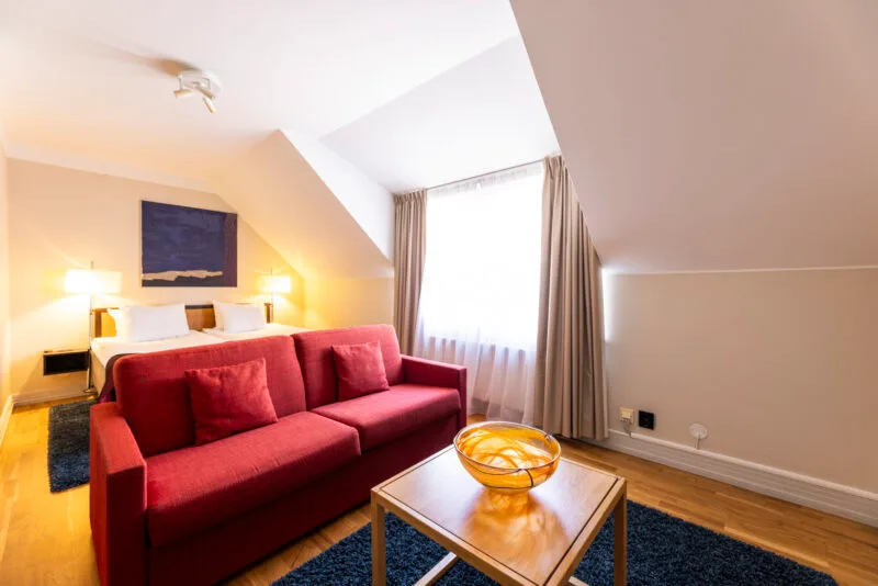 Modernt hotellrum med röd soffa, TV och fönster som släpper in naturligt ljus