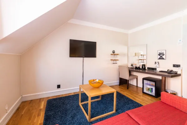 Rymligt hotellrum med röd soffa, skrivbord, minibar och väggmonterad TV