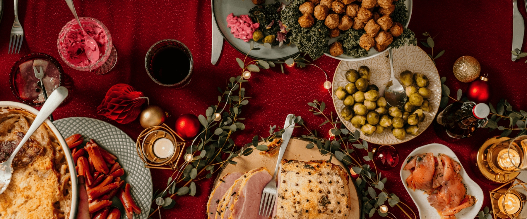 Julbord med olika rätter, röda bordsdekorationer och levande ljus