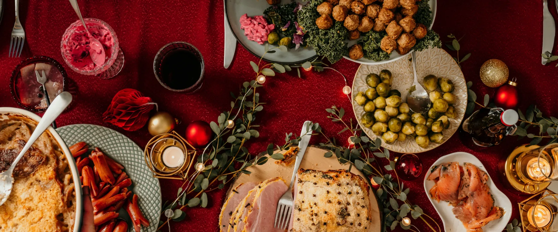 Julbord med olika rätter, röda bordsdekorationer och levande ljus