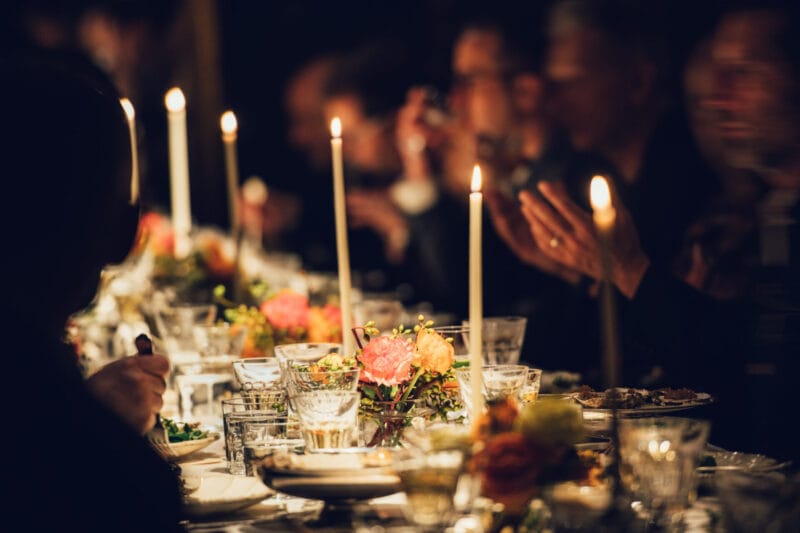 People enjoy a family dinner with candles. Big table served with food and beverages.