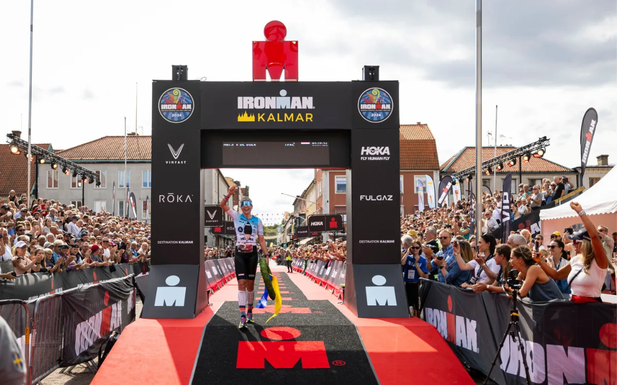 Ein Teilnehmer überquert die Ziellinie beim Ironman Kalmar 2024, umgeben von der Menge und den feiernden Zuschauern.