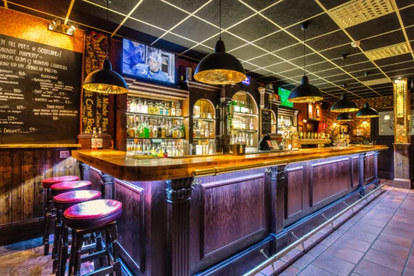 Bardisk med flaskor, glas och TV-skärmar i bakgrunden.