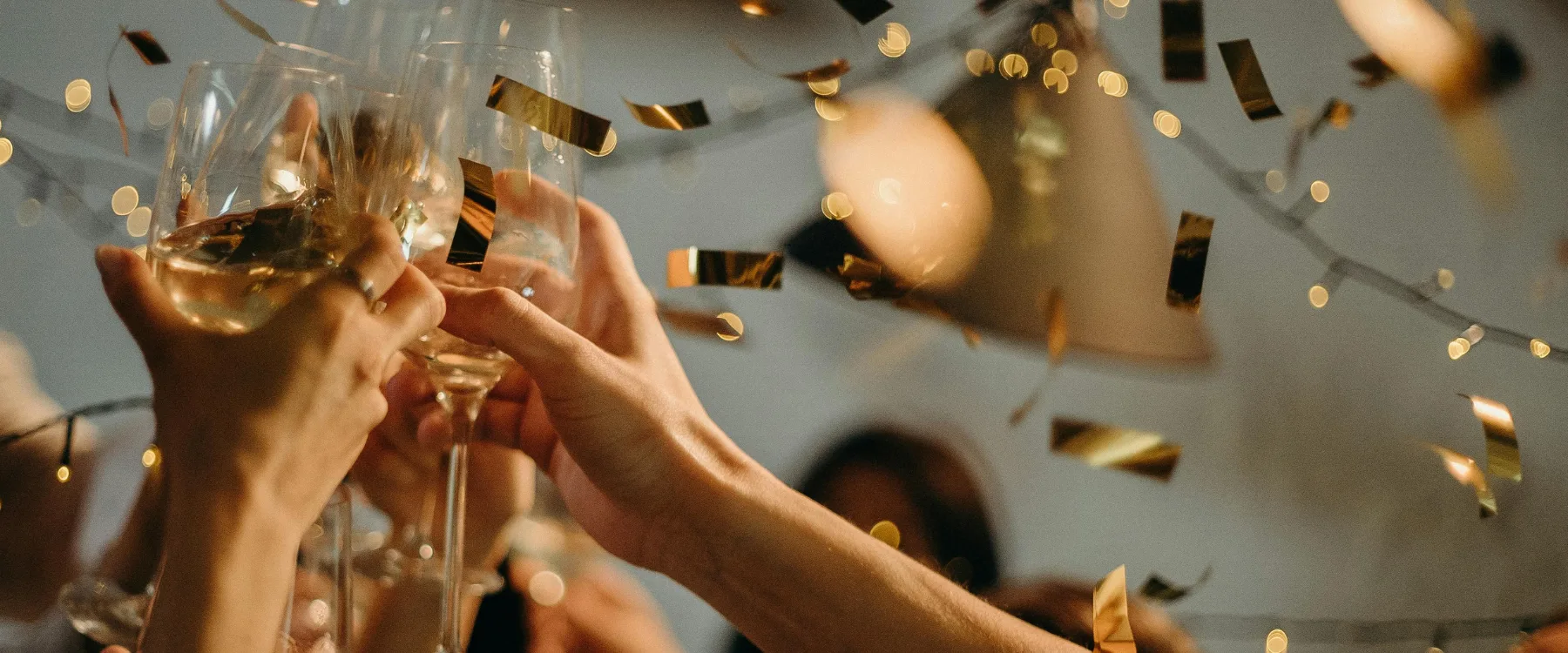Flera personer skålar med vinglas under en fest med konfetti och ljusslingor.
