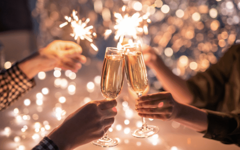 Personer skålar med champagneglas medan tomtebloss lyser i bakgrunden.