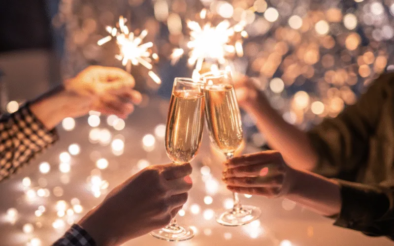 Personer skålar med champagneglas medan tomtebloss lyser i bakgrunden.