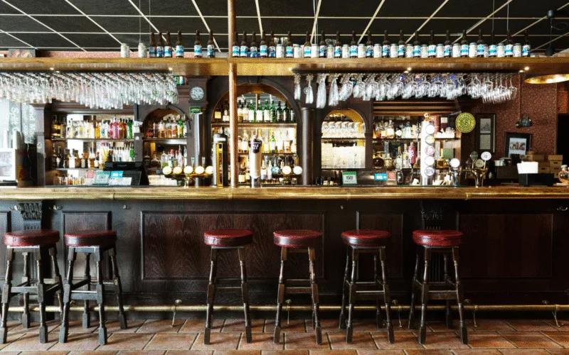 Barinteriör med höga barstolar och välfyllda hyllor med glas och flaskor.