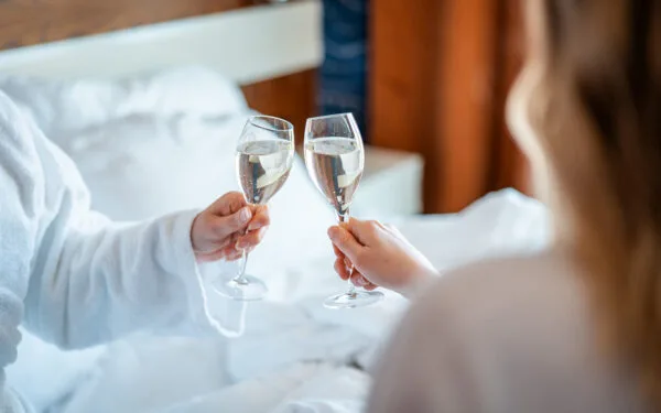 Två personer i morgonrock skålar med champagne medan de sitter i en säng.