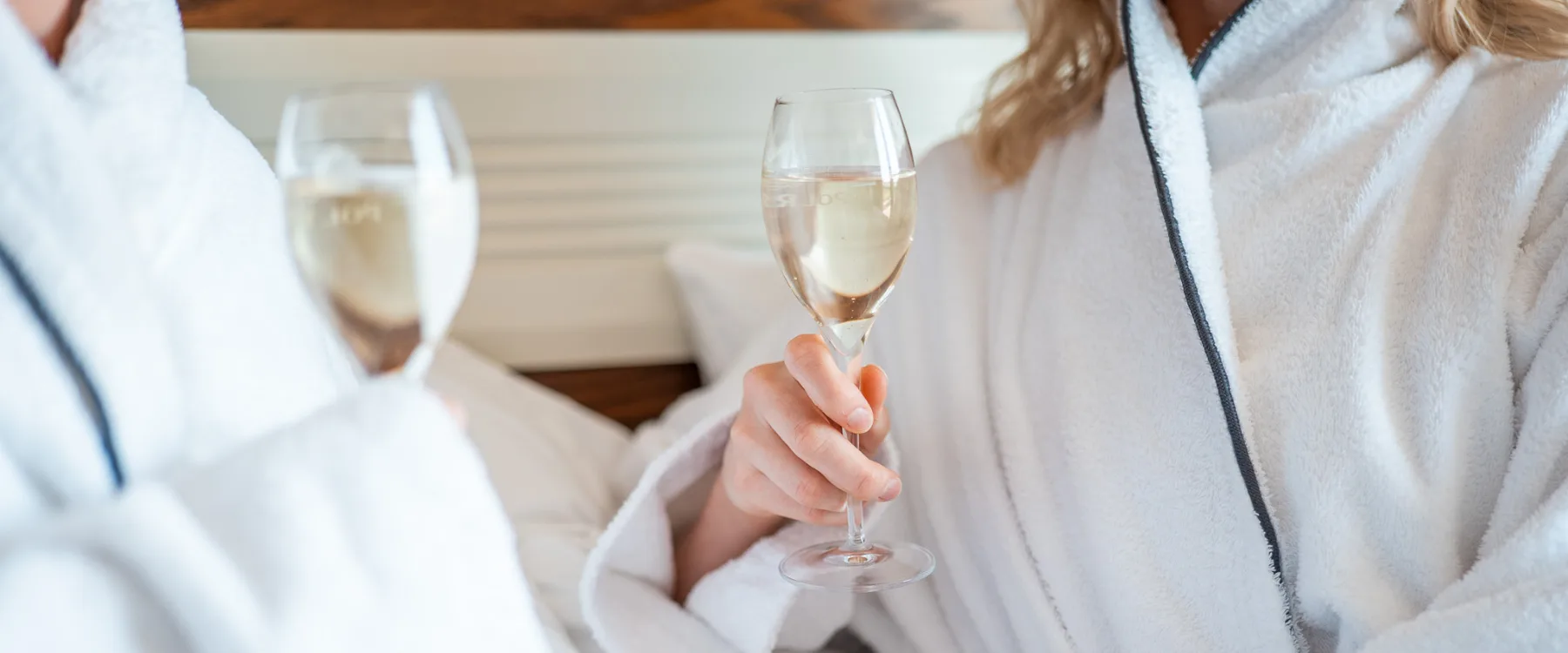 Par sitter i sängen i morgonrockar och skålar i bubbel