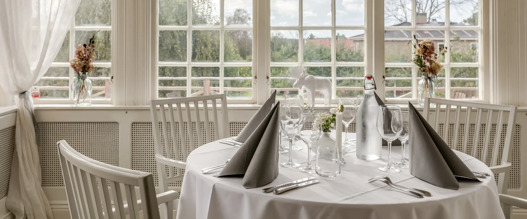 Ett dukat bord på en inglassad veraknda med sekelskiftsfönster.