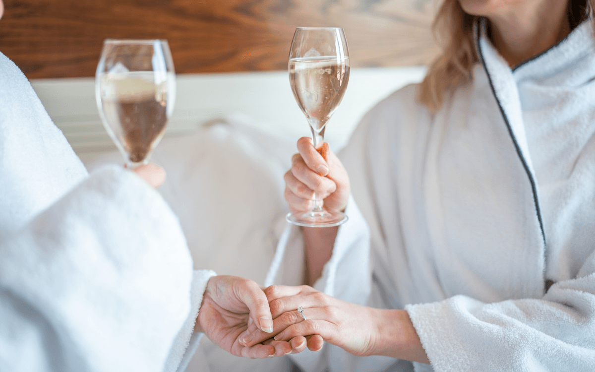 Ett gift par håller handen i mogonrockar på en säng.