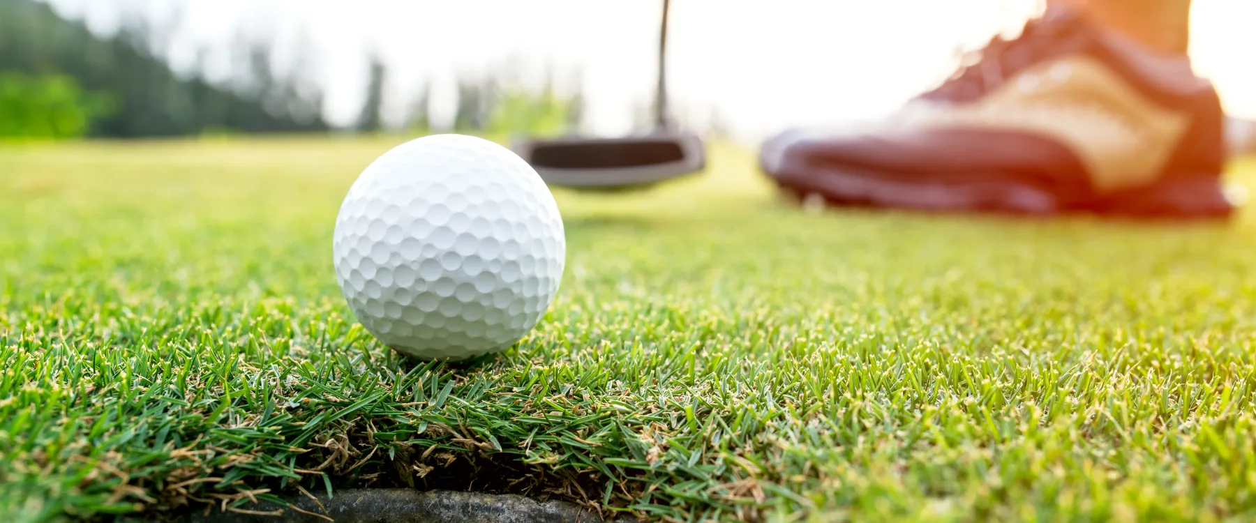 En golfboll i fokus med suddiga skor i bakgrunden.