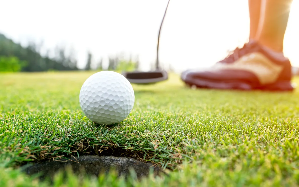 En golfboll i fokus med suddiga skor i bakgrunden.
