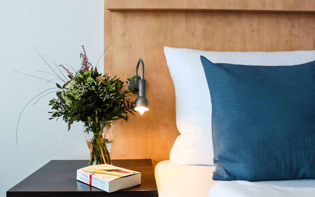 Hotelbett, Nachttisch mit Buch und Blumen