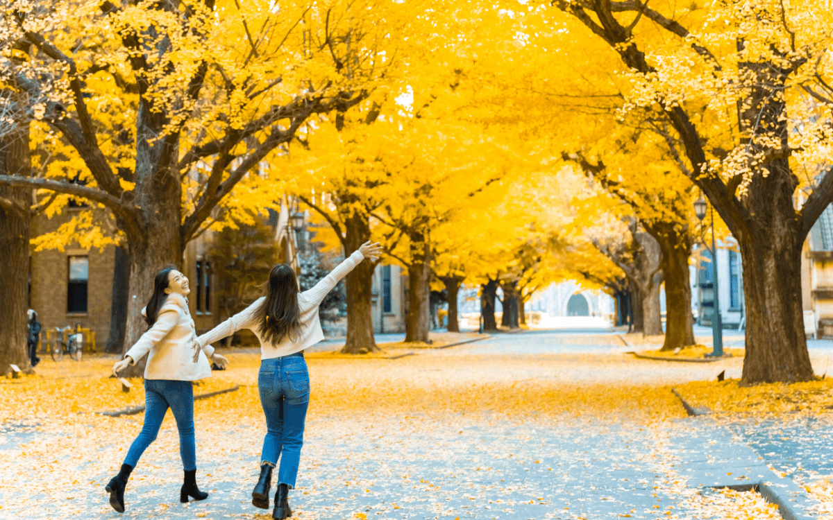two woman walking in a city with yellow leafed treas
